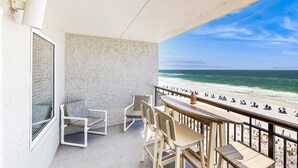 Ein Balkon mit Blick auf den Strand, inklusive Tisch, Stühlen und einem Fenster.