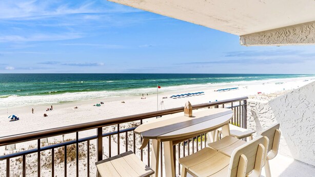 Ein Balkon mit Blick auf einen Strand, ausgestattet mit einem Tisch, Stühlen und einer Geländer.