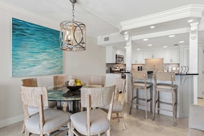 A modern kitchen with white cabinets, a central island, and a dining area with a glass table and wooden chairs. - Bright, beachfront condo with beach service included - quick walk to dining (Fort Walton Beach)