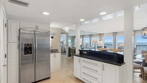 Een moderne keuken met een roestvrijstalen koelkast, witte kasten en een groot eiland met een zwart aanrecht.