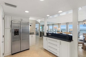 A modern kitchen with a stainless steel refrigerator, white cabinetry, and a large island with a black countertop. - Bright, beachfront condo with beach service included - quick walk to dining (Fort Walton Beach)