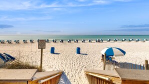 Een strand met rijen parasols en stoelen, een houten hek en een bord.