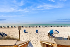 A beach with rows of umbrellas and chairs, a wooden fence, and a sign. - Bright, beachfront condo with beach service included - quick walk to dining (Fort Walton Beach)
