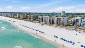 An aerial view of a beach resort with multiple high-rise buildings, a sandy beach, and clear turquoise waters. - Bright, beachfront condo with beach service included - quick walk to dining (Fort Walton Beach)