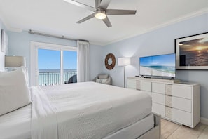 A hotel room with a bed, a ceiling fan, a TV, a dresser, a window with curtains, and a view of the ocean. - Bright, beachfront condo with beach service included - quick walk to dining (Fort Walton Beach)