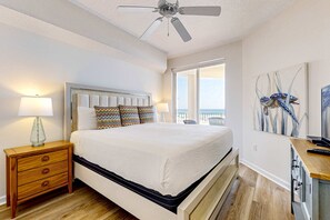 A bedroom with a bed, a nightstand, a ceiling fan, a window with a view, and artwork on the wall. - Gulf-front 3-bedroom condo with balconies off each bedroom & pickleball (Santa Rosa Beach)
