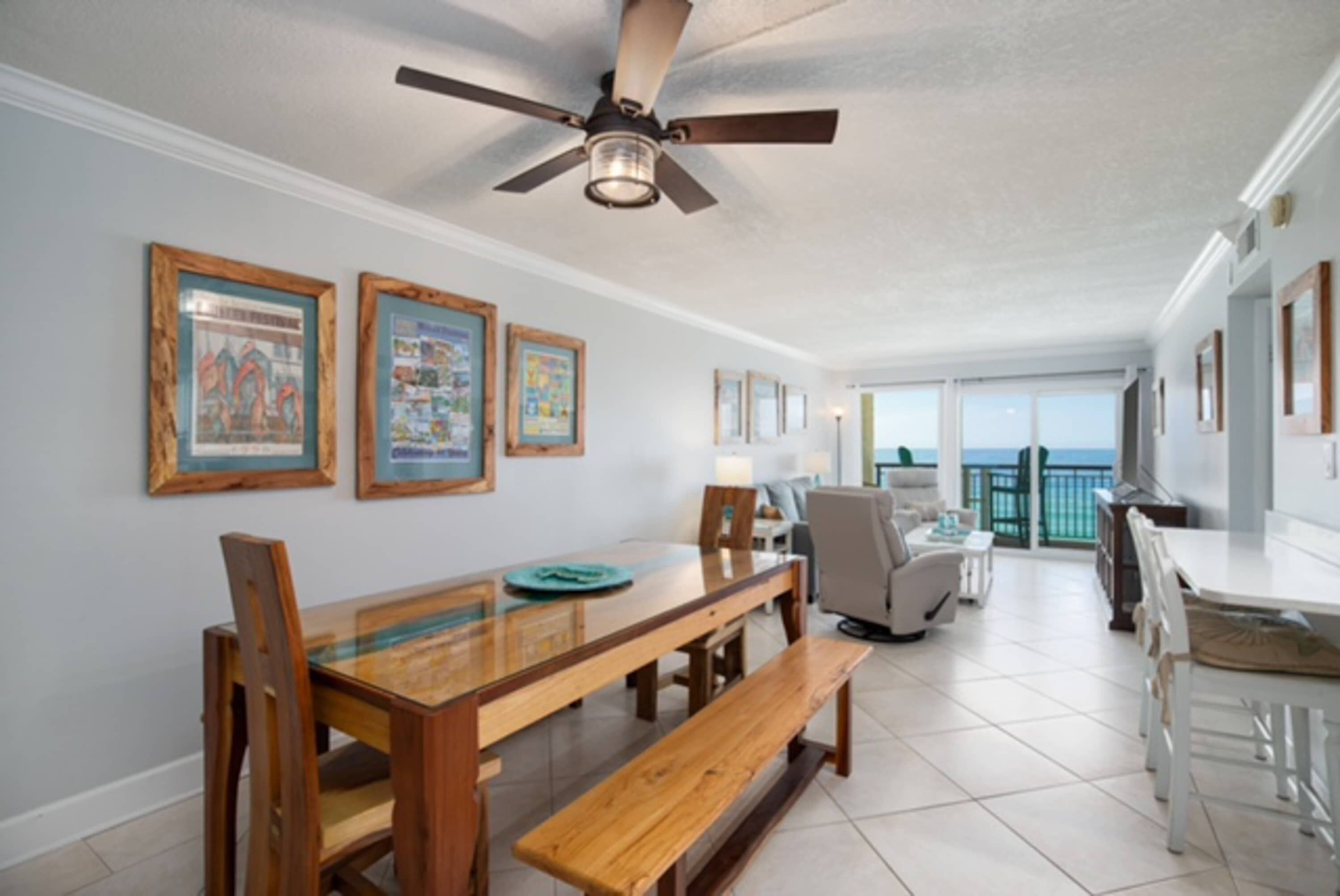 A dining area with a wooden table and benches, framed pictures on the wall, and a ceiling fan.