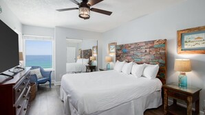 Ein Schlafzimmer mit einem großen Bett, einem Deckenventilator, einem Schminktisch, einem Stuhl und Blick aufs Meer.