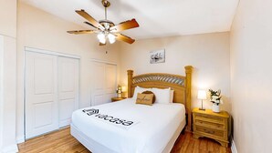 Un dormitorio con una cama, un ventilador de techo, una mesita de noche con lámpara y una puerta.