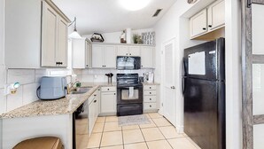 Una cocina con gabinetes blancos, un refrigerador negro, un microondas y una estufa.