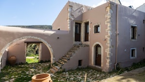 A building with a stone staircase leading to a door, a large arched entrance, and a small window. - Conaleni - Concona Houses (Rethymno)