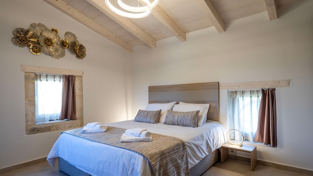 A bedroom with a large bed, a bedside table with a mirror, and decorative wall art. - Conaleni - Concona Houses (Rethymno)