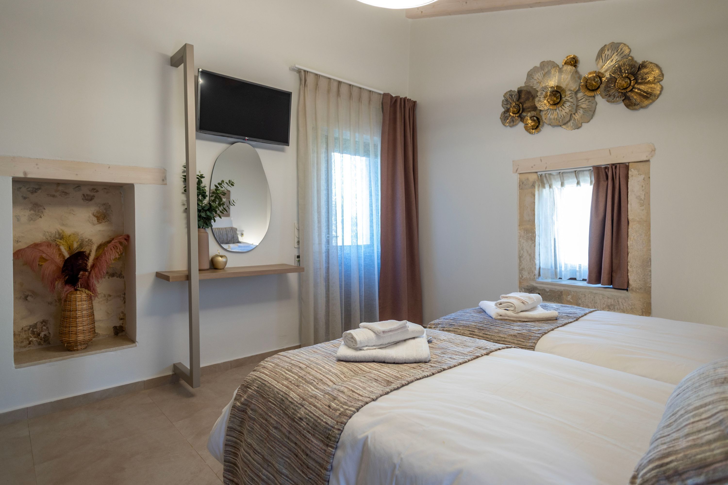 A hotel room with two beds, a TV, a mirror, a window with curtains, and decorative wall art.