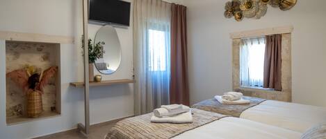 A hotel room with two beds, a TV, a mirror, a window with curtains, and decorative wall art.