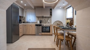 A modern kitchen with a built-in oven, dishwasher, and refrigerator. There is a dining area with wooden chairs and a table. - Conaleni - Concona Houses (Rethymno)