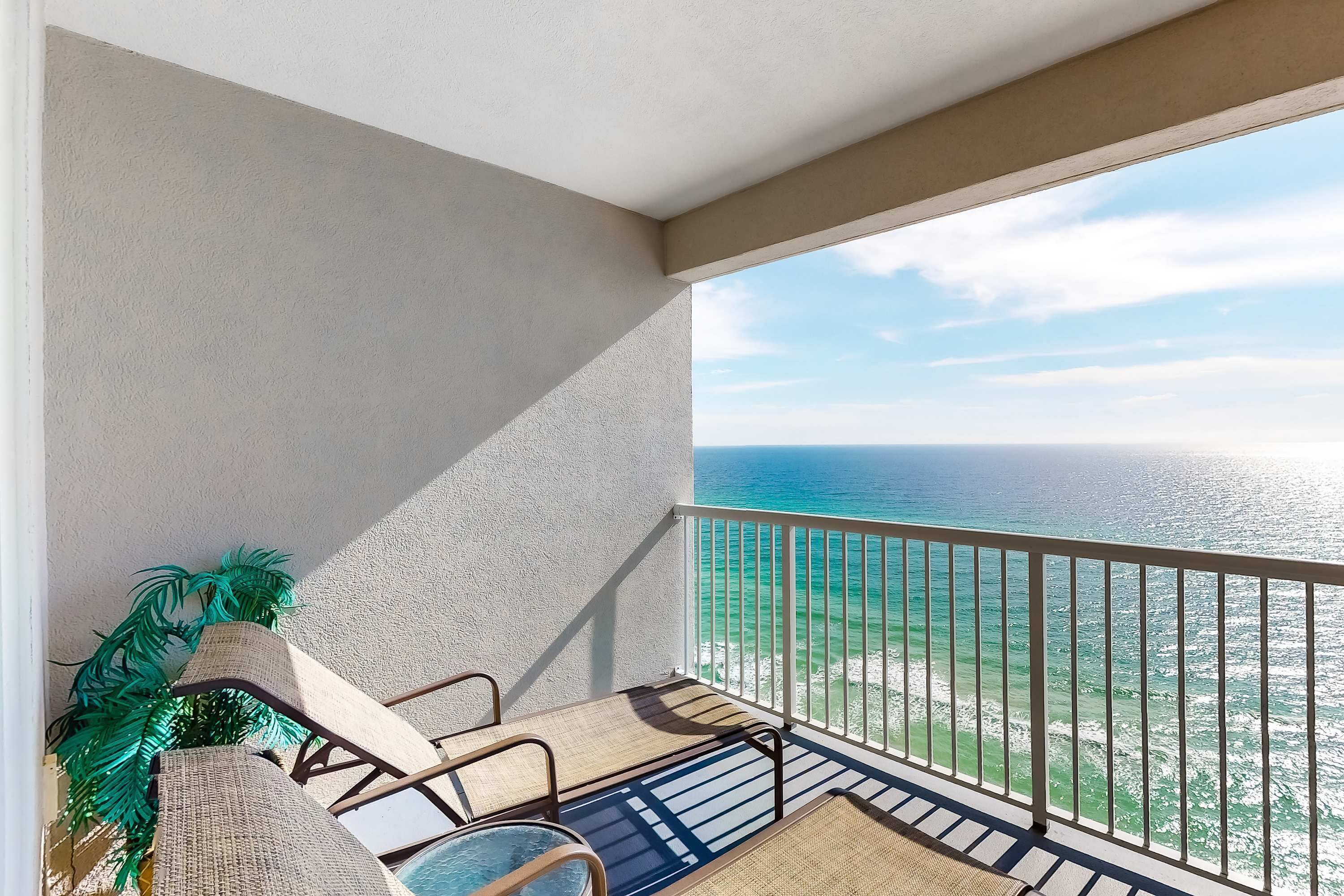 A balcony with a view of the ocean, wicker furniture, and a potted plant.