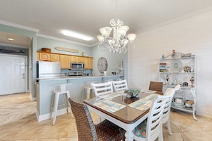 A dining area with a wooden table, white chairs, and a chandelier. - Top-floor penthouse condo with amazing view, balcony, W/D, pools, gym, & hot tub (Panama City Beach)