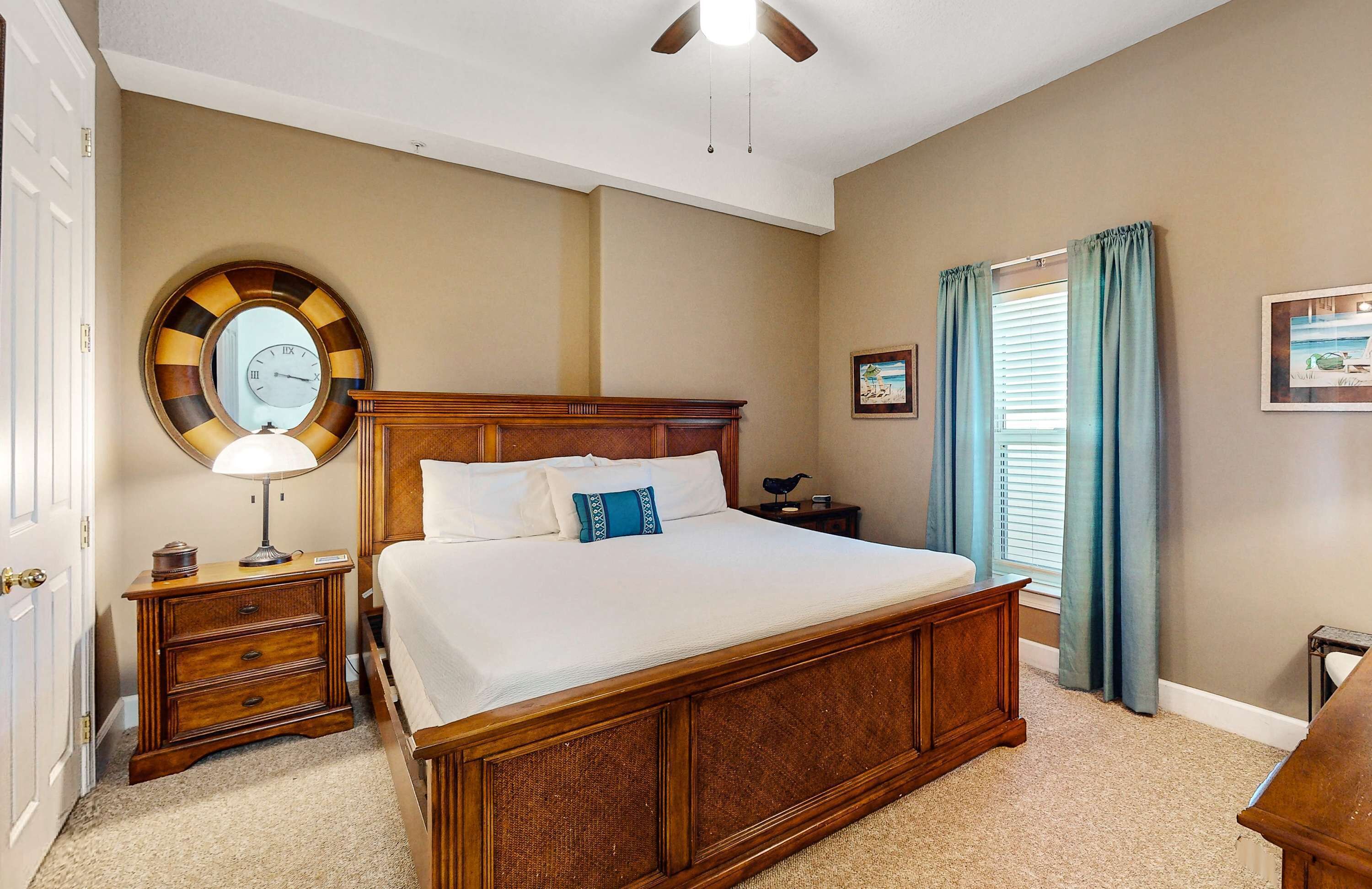 A bedroom with a wooden bed, a nightstand, a round mirror, and a window with curtains.