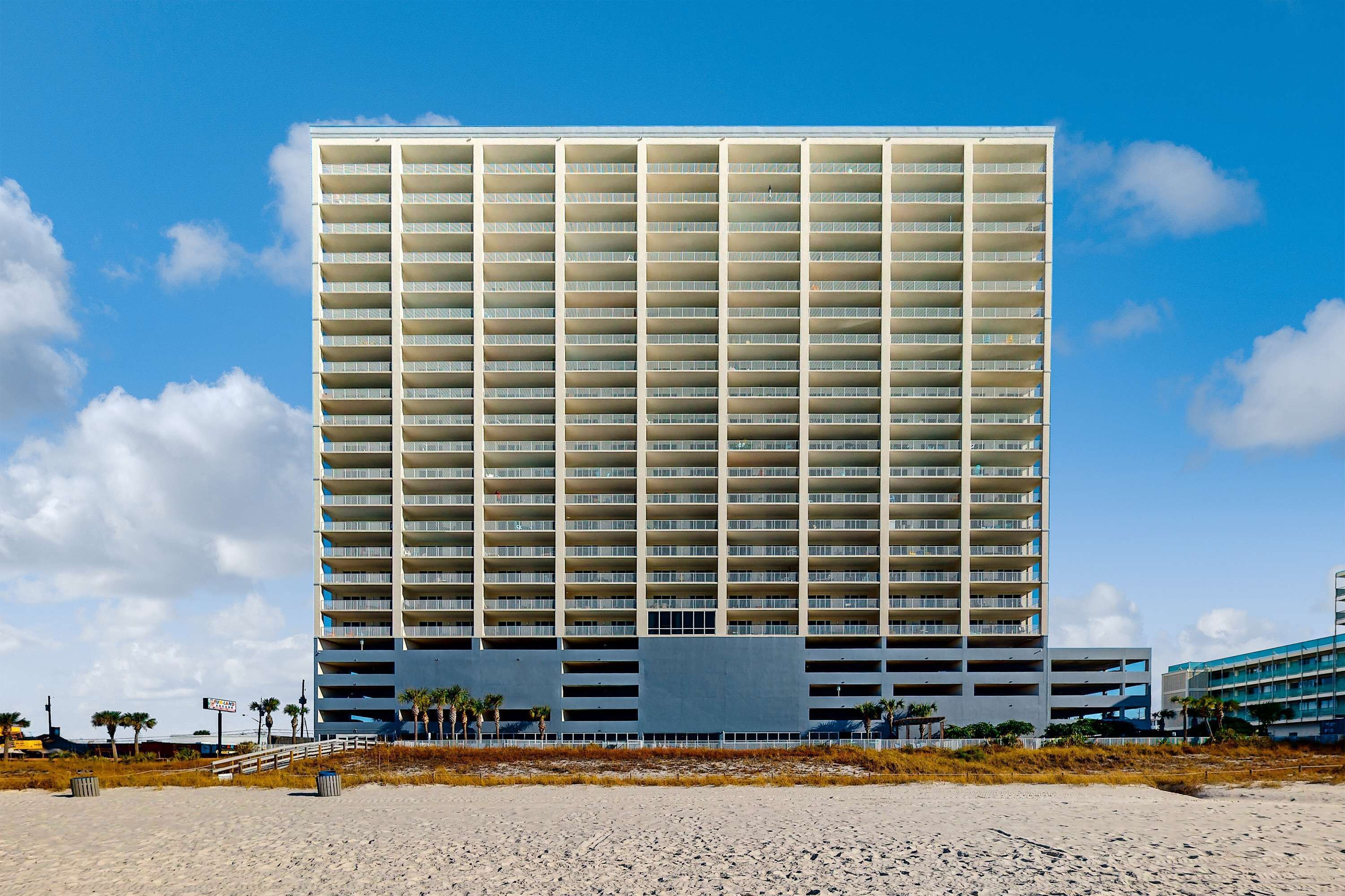 Un hotel de gran altura con varios pisos y balcones, situado cerca de una playa bajo un cielo despejado.
