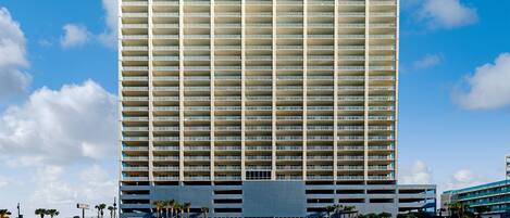 Un hotel de gran altura con varios pisos y balcones, situado cerca de una playa bajo un cielo despejado.