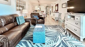 Un salon avec un canapé en cuir marron, un pouf bleu et un tapis à motifs.