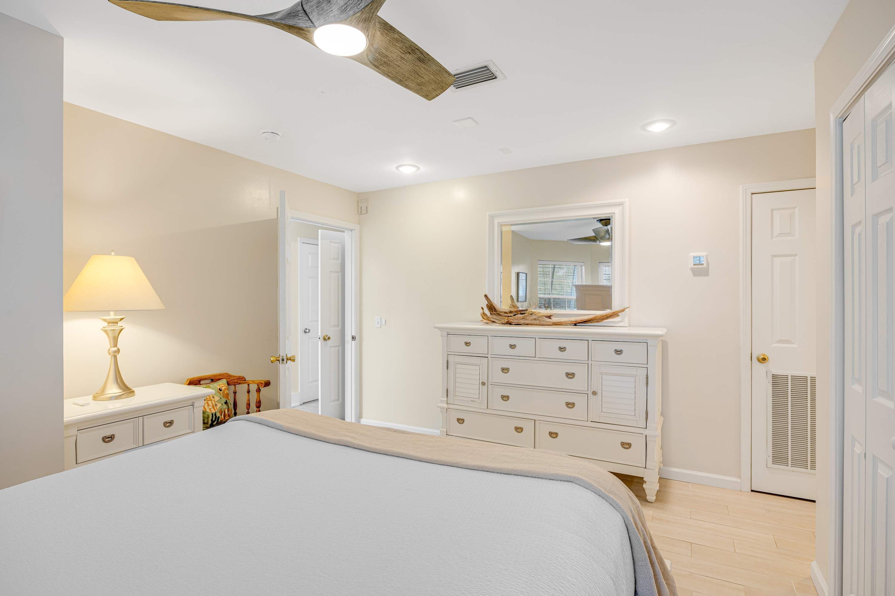 A bedroom with a bed, dresser, lamp, and ceiling fan.