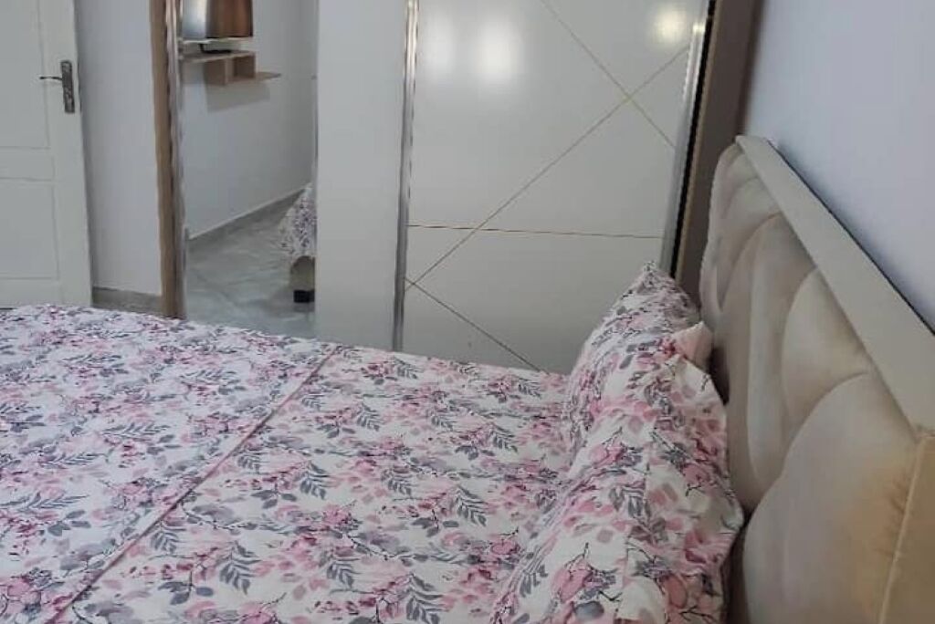 Un dormitori amb un llit, una porta i una petita estant.