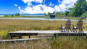 Een houten terras met stoelen en een tafel, in een gazon met uitzicht op een waterpartij en heuvels in de verte.