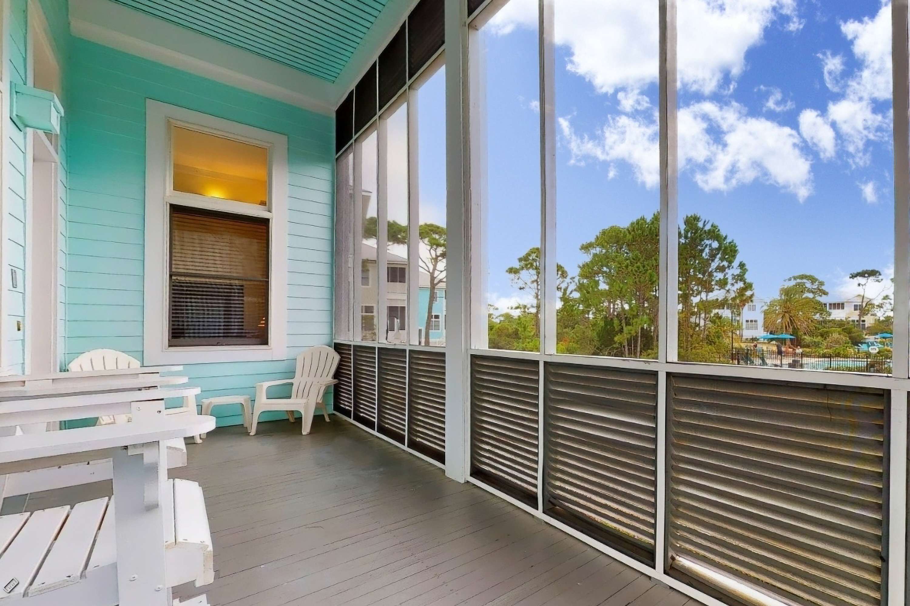 A turquoise exterior with a covered porch, white chairs, and a table.