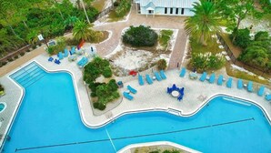 Luchtbeeld van een resort met een groot zwembad, ligbedden en palmbomen.