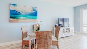 Ein Essbereich mit Korbstühlen, einem runden Tisch und einem Gemälde einer Strandansicht.