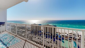 Ein Balkon mit Blick auf den Ozean und ein Parkbereich mit blauen Sonnenschirmen.