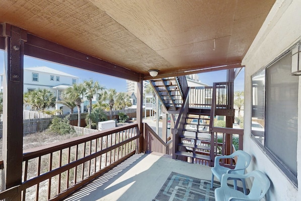 A covered outdoor area with a wooden railing, a staircase, and two plastic chairs. - Peaceful studio beach condo with shared pool & full W/D (Panama City Beach)