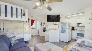 A compact living space with a sofa, a small table, a ceiling fan, a kitchenette, and a TV. - Peaceful studio beach condo with shared pool & full W/D (Panama City Beach)
