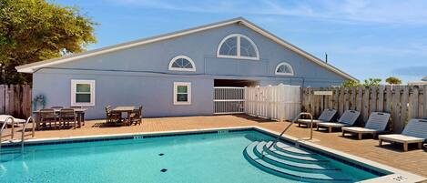 A swimming pool area with a pool, lounge chairs, and a building with a blue exterior.