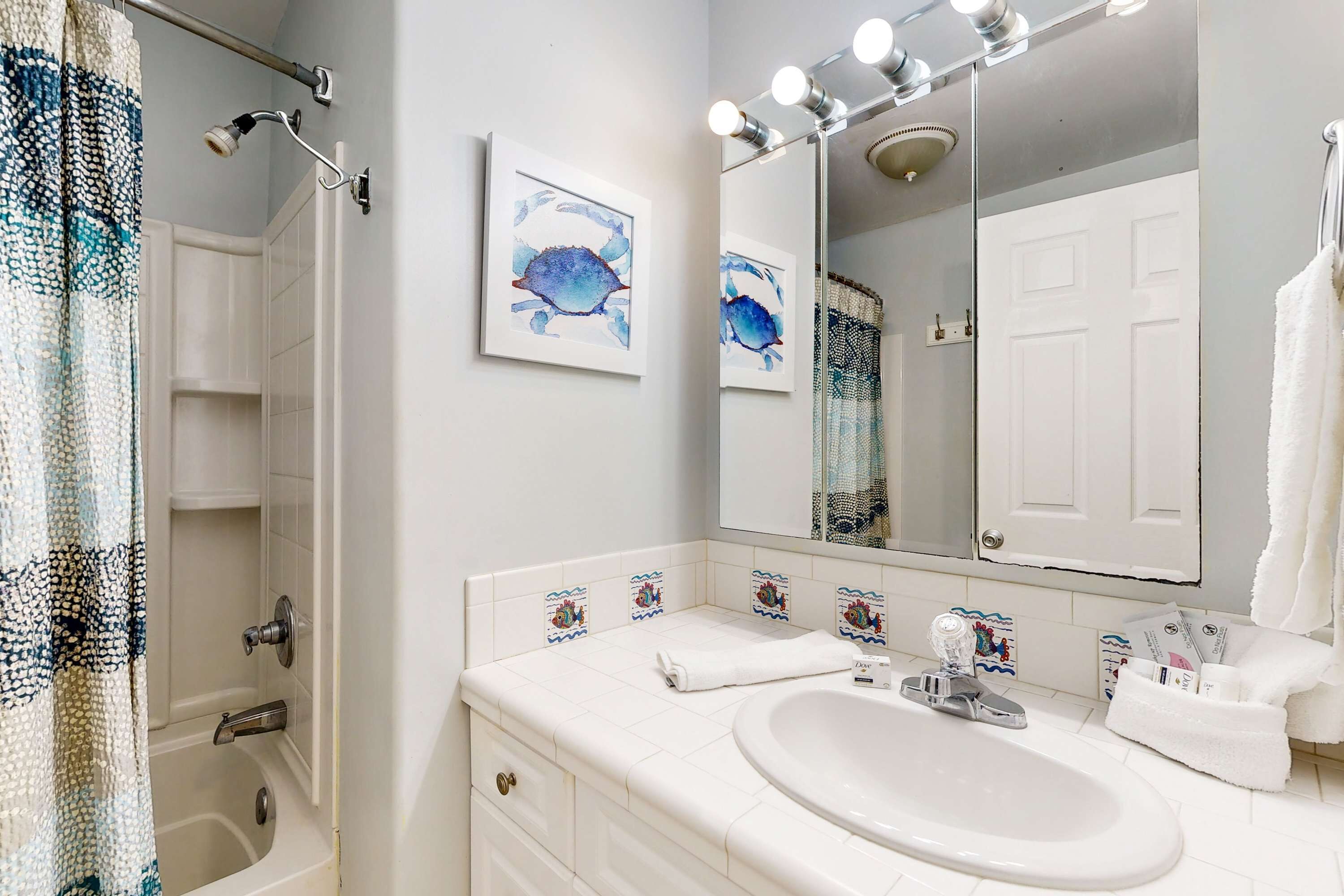 A bathroom with a bathtub, a sink, a mirror with lights, and a towel rack.