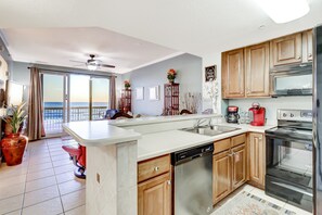 A modern kitchen with a dishwasher, oven, and a view of the ocean through the sliding glass door. - Dreamy retreat on the Gulf with pool, basketball court & beach access (Panama City Beach)