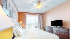 Un dormitorio con cama, cómoda, televisor, ventilador de techo y ventana con cortinas.