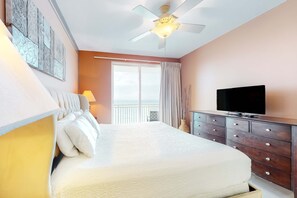 Ein Schlafzimmer mit einem Bett, einem Schminktisch, einem Fernseher, einem Deckenventilator und einem Fenster mit Vorhängen.