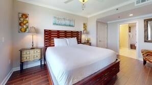 A bedroom with a large bed, a nightstand, a ceiling fan, and a painting on the wall. - Gulf-front condo with pool, hot tub, balcony, & complimentary beach service (Panama City Beach)