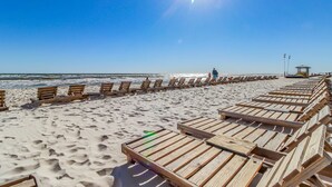 A beach with wooden lounge chairs aligned along the shore, a lifeguard tower, and the ocean in the background. - Gulf-front condo with pool, hot tub, balcony, & complimentary beach service (Panama City Beach)