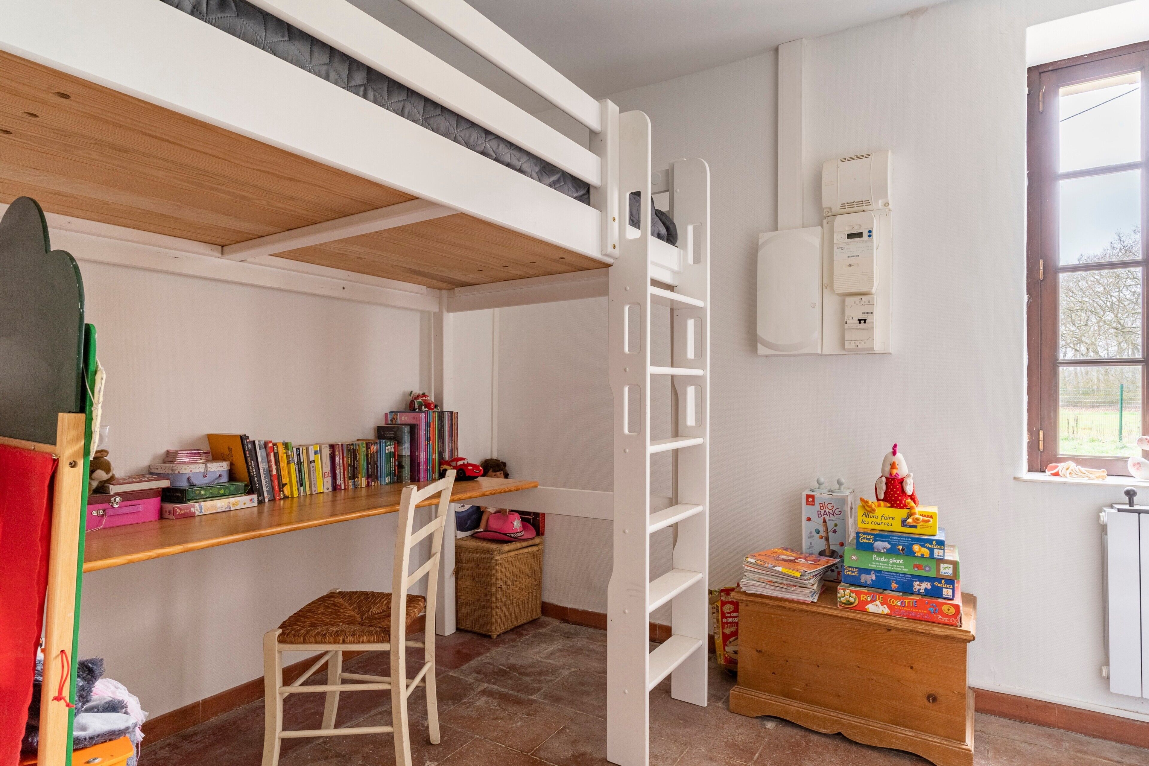 A child's bedroom with bunk beds, a desk, books, and a radiator.
