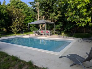 A rectangular swimming pool with a covered seating area and lounge chairs.