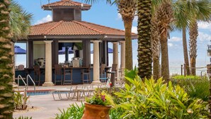 A poolside bar area with outdoor seating, palm trees, and a view of the ocean. - Beachfront retreat with pool, hot tub, gym, & seasonal beach chairs & umbrella (Panama City Beach)
