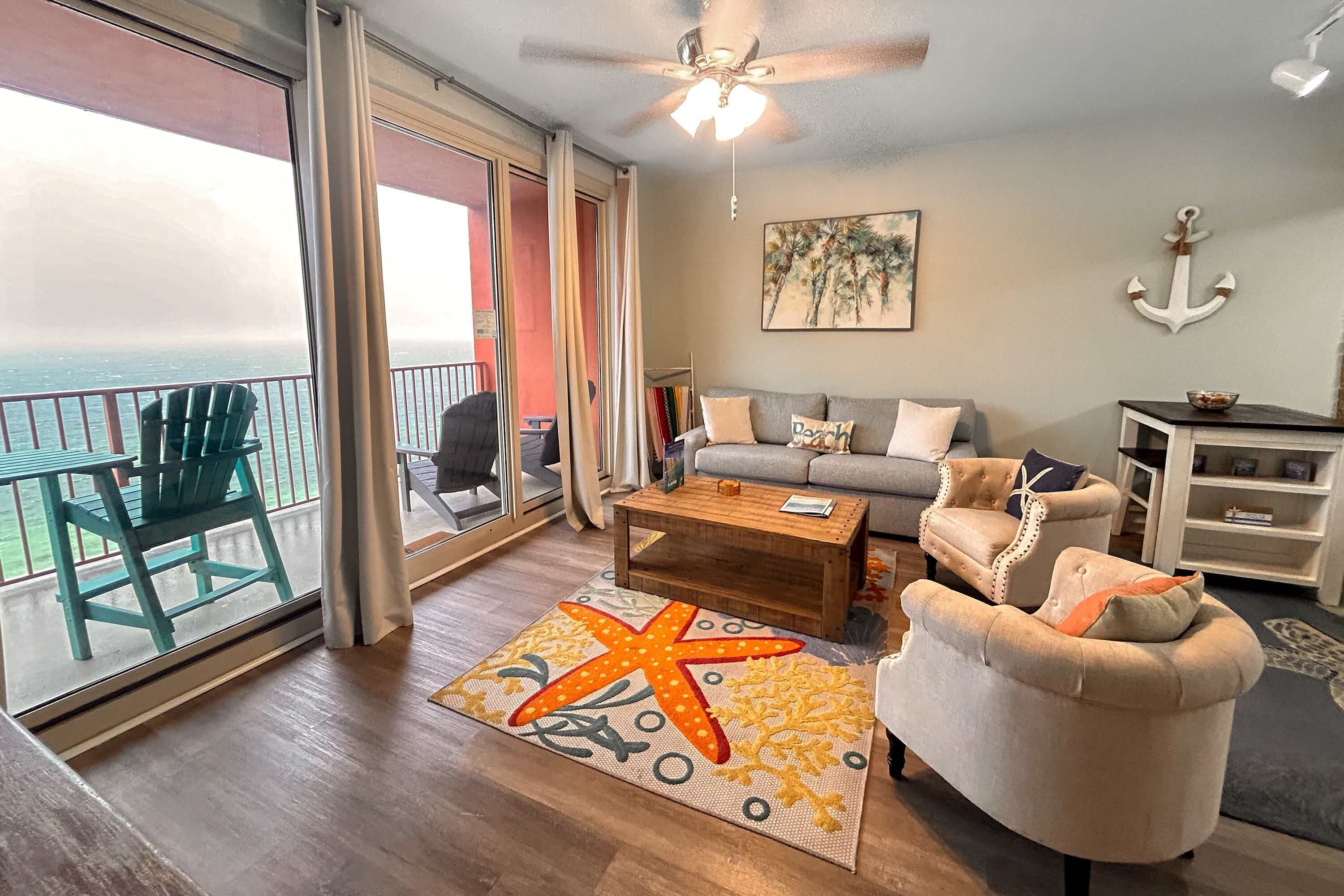 Ein geräumiges Wohnzimmer mit Balkon, Deckenventilator, einer Couch, einem Couchtisch und einem Teppich mit Sternfischmuster.