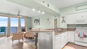 A modern kitchen with a central island, white cabinets, and a view to the outside. - Beachfront retreat with pool, hot tub, gym, & seasonal beach chairs & umbrella (Panama City Beach)
