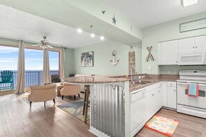 A modern kitchen with a central island, white cabinets, and a view to the outside. - Beachfront retreat with pool, hot tub, gym, & seasonal beach chairs & umbrella (Panama City Beach)