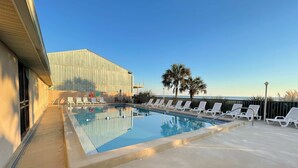 A swimming pool with lounge chairs, a building with a metal facade, and palm trees. - Beachfront Townhouse w/ Modern Upgrades Shared Pool, Fast WiFi, Outdoor Shower (Panama City Beach)