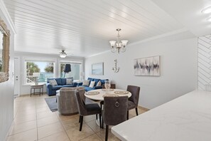 A spacious living area with a dining table, blue sofas, and a ceiling fan. - Beachfront Townhouse w/ Modern Upgrades Shared Pool, Fast WiFi, Outdoor Shower (Panama City Beach)