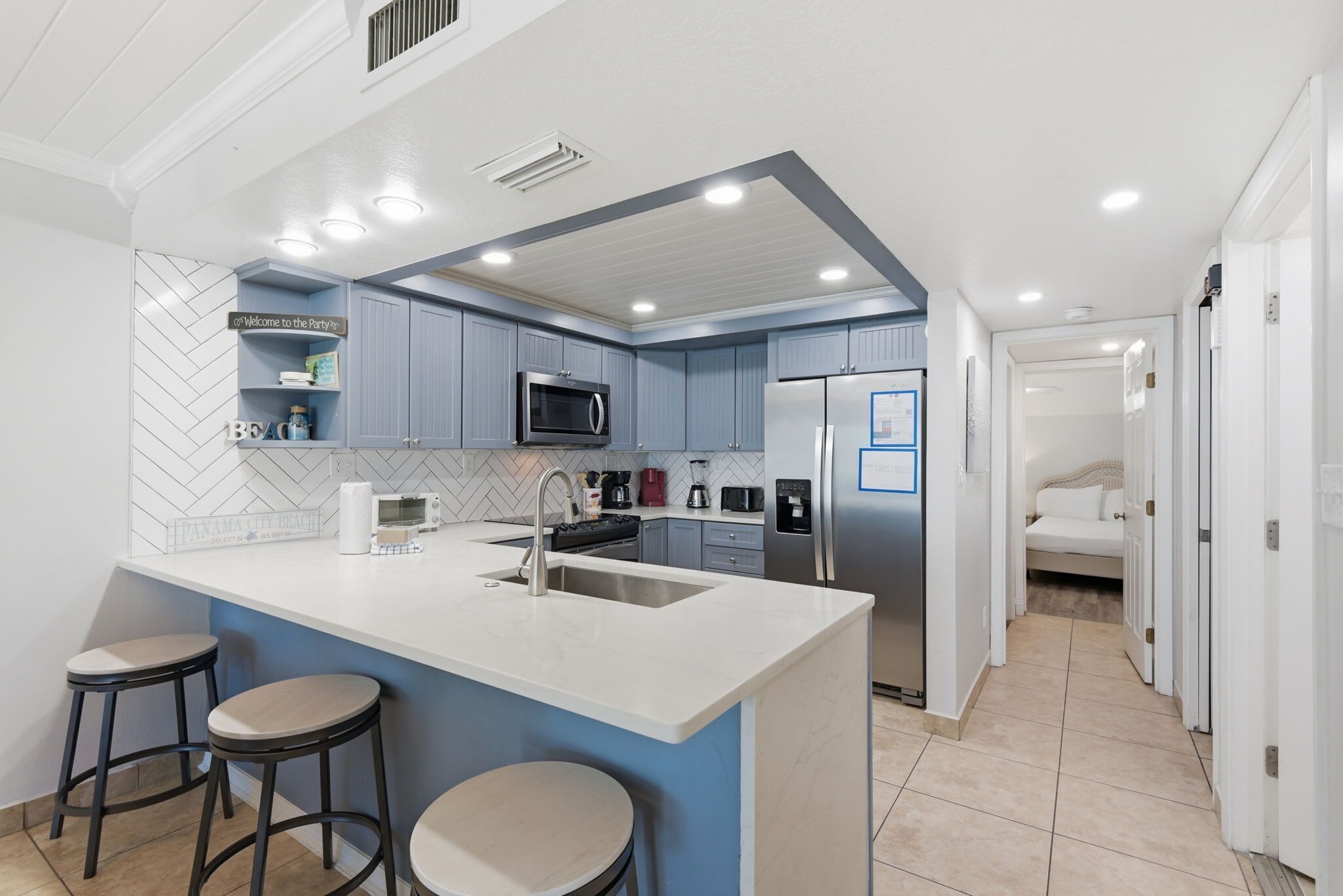 Una cocina moderna con una isla central, taburetes de bar, microondas, refrigerador y cafetera.